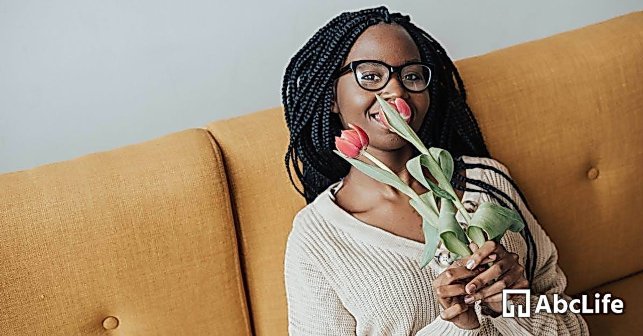 Happy black lady with flowers in hands on sofa