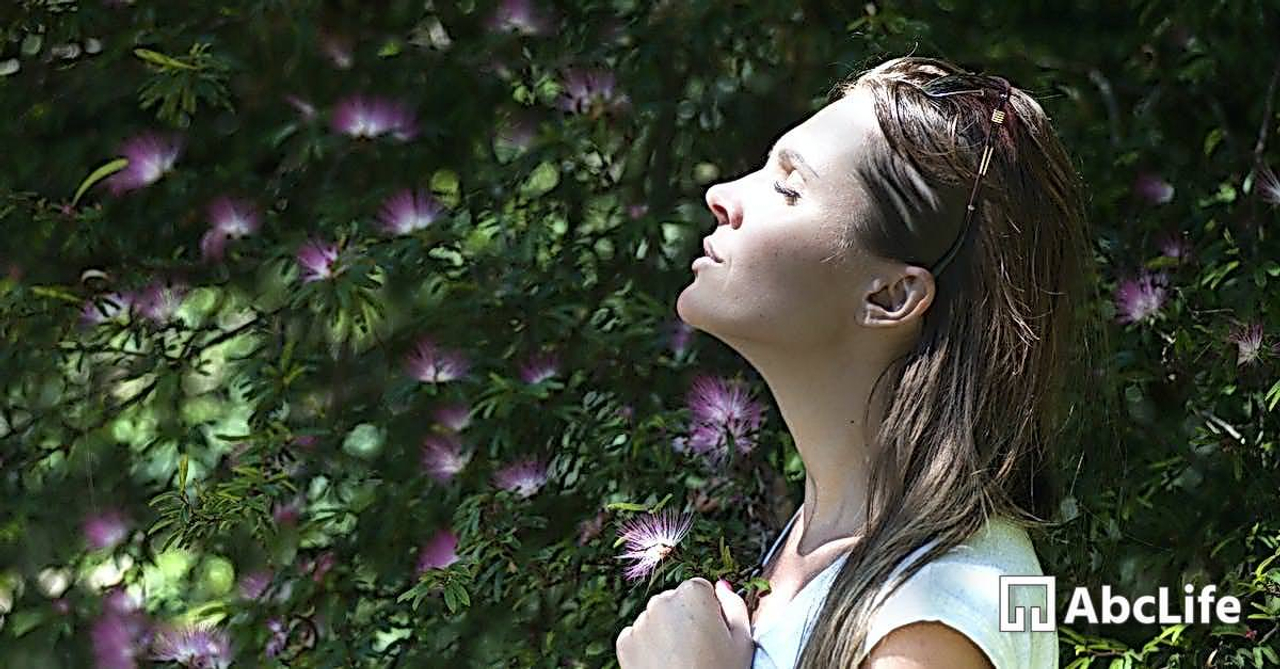 Woman Closing Her Eyes Against Sun Light Standing Near Purple Petaled Flower Plant