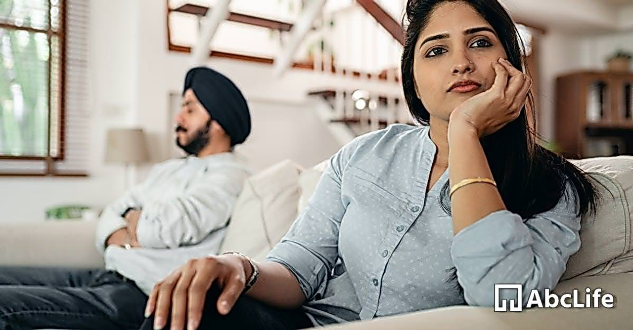 Sad young Indian woman avoiding talking to husband while sitting on sofa