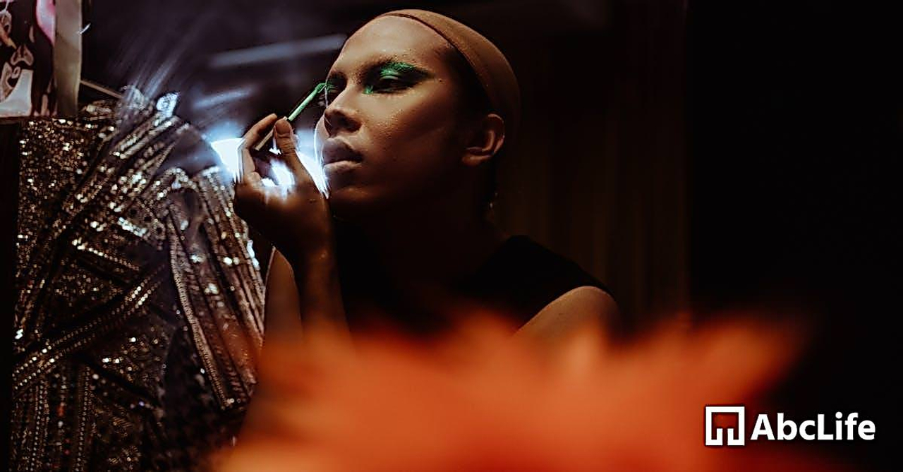 Young focused ethnic female theater artist applying eye shadow on eyelid with cosmetic brush in shiny dressing room